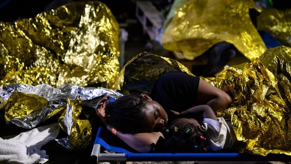 Eine Frau und ein Kind schlafen vor dem Aufnahmezentrum für Migranten. Der Stadtrat der italienischen Mittelmeerinsel Lampedusa hat angesichts Tausender neu angekommener Bootsmigranten den Notstand ausgerufen. © dpa Foto: Valeria Ferraro
