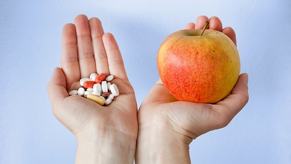 Zwei Hände halten einen Apfel und einige Tabletten. © Fotolia Foto: monropic