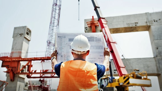 Ein Bauarbeiter schaut sich einen Bauplan auf einer Baustelle an. © fotolia Foto: Rawpixel.com