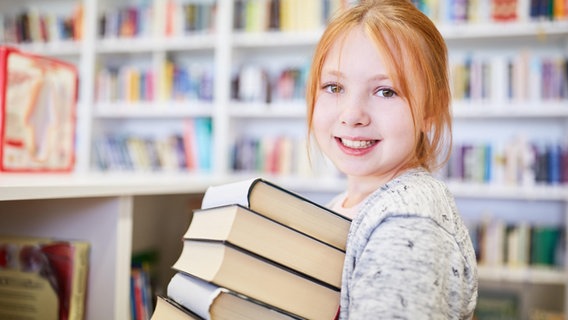 Ein lächelndes Mädchen trägt einen Stapel Bücher. © picture alliance / Zoonar | Robert Kneschke Foto:  Robert Kneschke