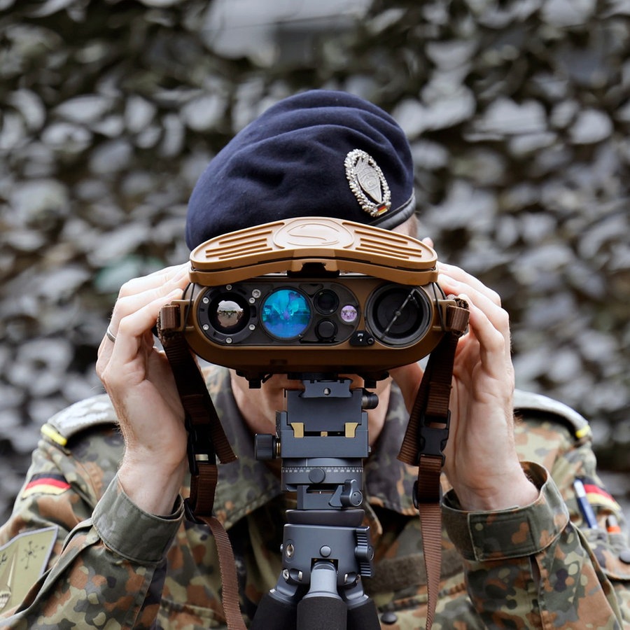 Ein Soldat blickt durch ein militärisches Fernglas vor Tarnnetzen in der Systemschau CIR-Fähigkeiten. © picture alliance / Panama Pictures Foto: Christoph Hardt