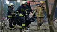 Auf diesem vom Staatlichen Katastrophenschutz der Ukraine zur Verfügung gestellten Foto tragen Feuerwehrleute eine Leiche nach einem, nach ukrainischen Angaben, russischen Luftangriff. © State Emergency Service of Ukrai/AP/dpa 