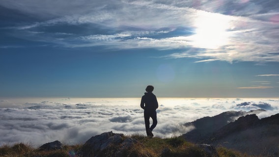 Eine Person steht in den Bergen einsam über einem Meer von Wolken © picture alliance / CHROMORANGE | Michelangelo Oprandi Foto: Michelangelo Oprandi