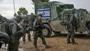 Israelische Soldaten stehen neben Militärfahrzeugen, während sie sich an einem Sammelpunkt nahe der Grenze zum Gazastreifen vorbereiten. © AP/dpa Foto: Ohad Zwigenberg