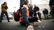 Ein Klimaaktivist hat sich an einer Hauptverkehrsstraße mit der Hand auf den Asphalt geklebt. © dpa Foto: Bernd Thissen