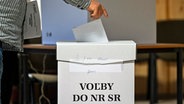 Ein Mann steckt bei den vorgezogenen Parlamentswahlen in der Slowakai seinen Stimmzettel in eine Wahlurne. © TASR/dpa Foto: Jaroslav Novák