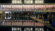Menschen stehen unter einer Leuchtschrift mit dem Text "Bring Them Home" (Bringt sie nach Hause), bei einer Demonstration, die die Rückkehr der Geiseln fordert, die bei dem Hamas-Angriff vom 07.10.2023 in Israel entführt wurden. © AP/dpa Foto: Ohad Zwigenberg