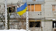 Die Nationalflagge der Ukraine steht vor einem zerstörten Gebäude in Borodjanka. © BELGA/dpa Foto: Pool Philip Reynaers