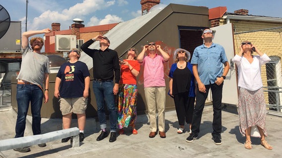 Einige Mitarbeiter des ARD Studio Washington stehen auf dem Dach des Hauses. Mit Sonnenbrillen schauen sie während der totalen Sonnenfinsternis in die Sonne. © ARD Studio Washington 