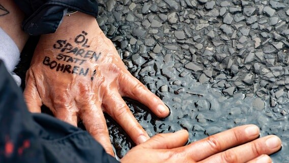 "Öl sparen statt bohren!" steht auf der Hand einer Demonstrantin der Gruppe "Letzte Generation", die sich auf dem Asphalt festgeklebt hat. © picture alliance/dpa Foto: Paul Zinken