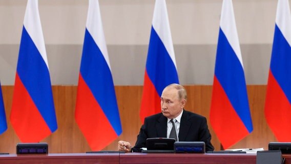 Der russische Präsident Wladimir Putin sitzt an einem Tisch, hinter ihm stehen mehrere russische Flaggen. © Uncredited/POOL TASS Host Photo Agency/AP/dpa 