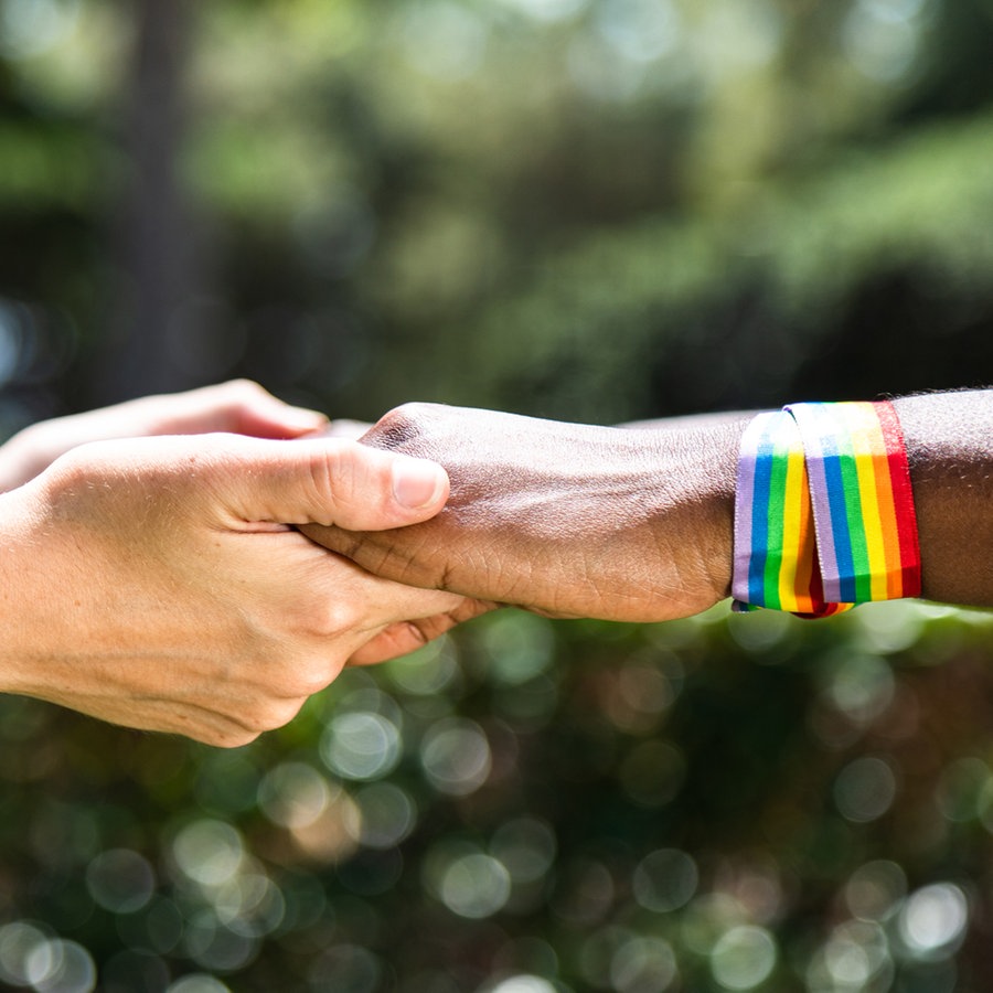 Zwei Menschen mit Regenbogenarmbändern halten sich an den Händen © Colourbox Foto: #311807