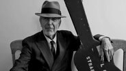 Leonard Cohen mit Hut und dem Arm auf dem Gitarrenkoffer. © picture alliance 