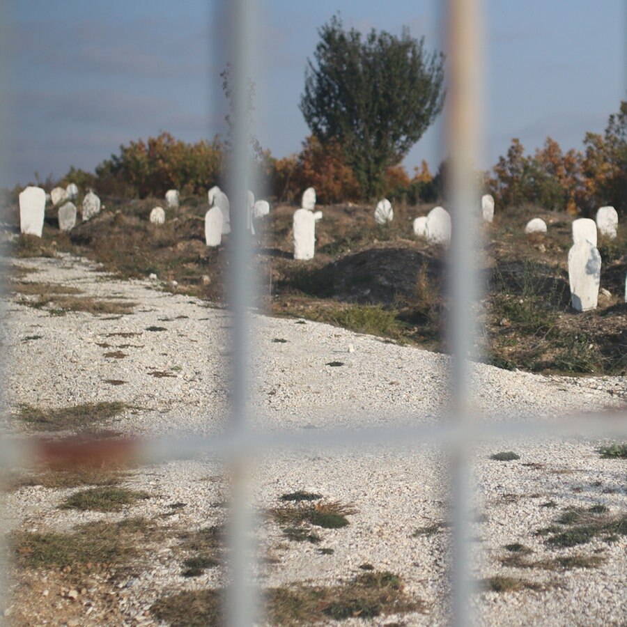 Hinter einem Gitterzaun sind viele schlichte Grabsteine auf Sandboden sichtbar. © ARD Foto: Rüdiger Kronthaler