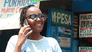 Eine Frau telefoniert mit einem Mobiltelefon in Nairobi, dahinter ein M-PESA Schriftzug. © ARD Foto: Antje Diekhans