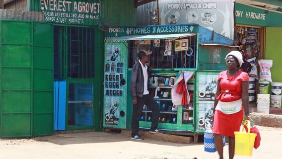 Eine kleines Geschäft für Mobiltelefone und Accessoires, davor eine Frau mit Taschen. © ARD Foto: Antje Diekhans