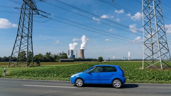 Auf einer Straße fährt ein Auto, im Hintergrund sind die Braunkohlekraftwerke Niederaußem und Neurath zu sehen. © dpa picture alliance Foto: Jochen Tack