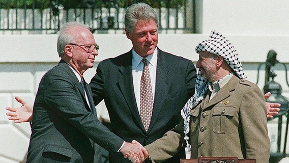Israels Premierminister Jitzchak Rabin (li.) und Palästinenser-Präsident Jassir Arafat (re.) bei dem historischen Händeschütteln am Weißen Haus - zusammengeführt von US Präsident Bill Clinton (1993). © picture alliance Foto: Avi_Ohayon-Israeli_Government_Pr