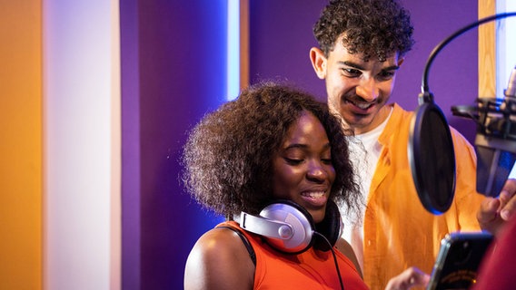 Eine Frau und ein Mann mit Kopfhörern und Smartphone in einem Studio (Symbolfoto). © Imago Foto: David Munoz