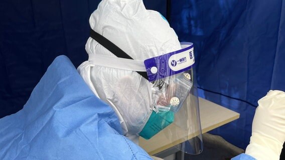 Eine mit Schutzkleidung gegen eine Coronavirus-Übertragung gekleidete Person bei einem Coronatest. © ARD Foto: Eva Lamby-Schmitt