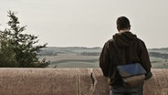 Ein Mann steht vor einer Betonbrüstung und schaut in die Landschaft. © Photocase Foto: Susann Städter