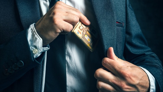 Ein Mann steckt sich Geldscheine in die Innentasche seines Jacketts. © Fotolia Foto: Igor Stevanovic