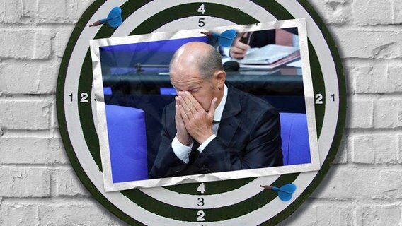 Eine Bildmontage zeigt eine Postkarte auf einer Dartscheibe. Sie zeigt Bundeskanzler Olaf Scholz, der sich die Hände vors Gesicht hält. © Imago / Political-Moments Foto: Imago