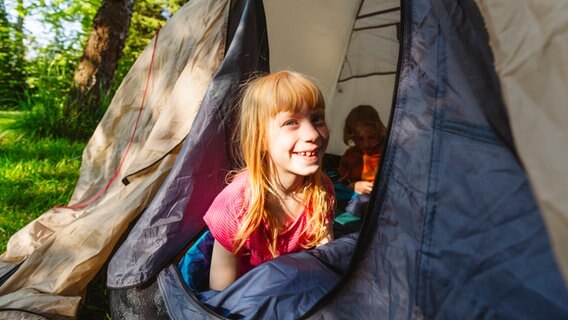 Ein Mädchen sitzt in einem Zelt © IMAGO / Westend61 