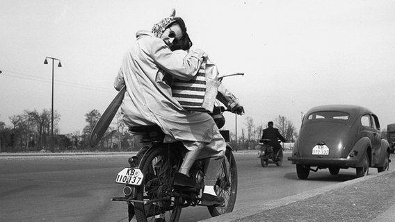 Eine junge Frau auf dem Rücksitz eines Mopeds hält ein Paddel unter dem Arm. © picture-alliance / akg-images Foto: akg-images / Horst Maack