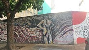 Ein Wand-Graffiti in Buenos Aires auf einer Mauer stellt den Musiker Carlos Gardel dar, davor steht ein Baum © NDR Foto: Christine Siebert