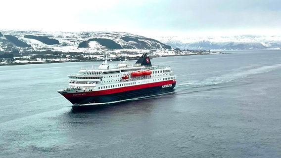 Ein weiß rotes Schiff fährt durch einen Fjord in der Landschaft der Hurtigruten in Norwegen, dahinter eine Landschaft mit Schnee © NDR Foto: Wiebke Keuneke / Mark Diening