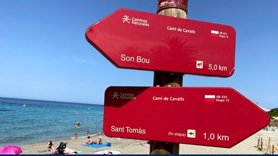 Zwei rote Schilder am Strand von Menorca weisen auf Wanderpfade hin. © NDR Foto: Carsten Vick