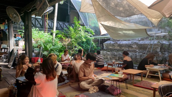 Menschen sitzen auf dem Boden an Tisschen im Artisthouse Baan Silapin in Thailand © NDR Foto: Isa Hoffinger