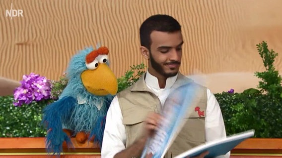 Szene aus einer Sesamstraßenfolge: Ein Papagei sitzt auf der Schulter eines junges Mannes (Screenshot).  