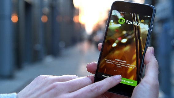 Eine Hand hält ein Smartphone, auf der die App von Spotify angezeigt wird. © dpa picture alliance Foto: Britta Pedersen