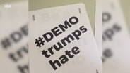 Ein Zettel mit der Aufschrift "#demo trumps hate" liegt auf einem Tisch. © NDR 