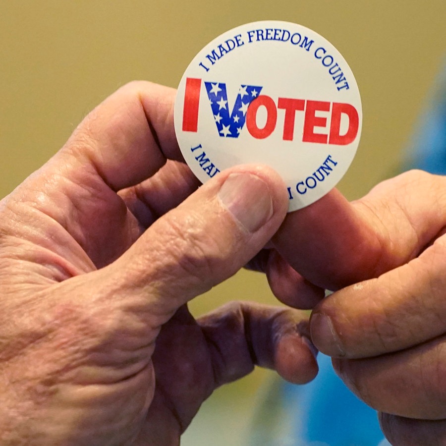 USA: Gary Wilson (r), Wahlhelfer in einem Wahllokal in Rankin County, überreicht einer Person, die einen Stimmzettel ausgefüllt hat, einen "Ich habe gewählt"-Aufkleber. © Rogelio V. Solis/AP/dpa 