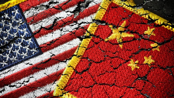 Die Fahnen von USA und China liegen übereinander, sie sind als Bruchstücke abgebildet. © dpa picture alliance/chromorange Foto: Christian Ohde