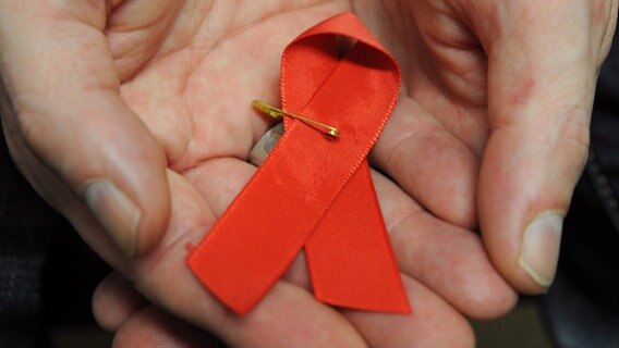 Ein Mann hält eine rote Schleife als Symbol der Solidarität mit HIV-Positiven und Aids-Kranken. © dpa Foto: Arne Dedert