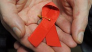 Ein Mann hält eine rote Schleife als Symbol der Solidarität mit HIV-Positiven und Aids-Kranken. © dpa Foto: Arne Dedert