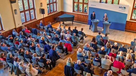 Mecklenburg-Vorpommerns Ministerpräsidentin Schwesig steht auf einer Bühne. Vor ihr sitzen auf mehreren Stuhlreihen Bürgerinnen und Bürger. © dpa Foto: Jens Büttner
