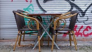Zwei Stühle und ein Cafètisch stehen angeschlossen vor einer verschlossenen Gastronomie © IMAGO / Seeliger Foto: IMAGO / Seeliger