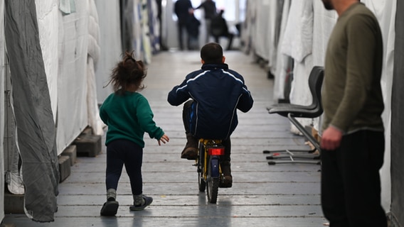 Flüchtlinge sind in einem der Zelte einer provisorischen Flüchtlingsunterkunft unterwegs. © dpa Foto: Arne Dedert