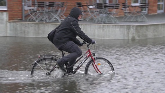 Ein Radfahrer fährt in Wismar durch das Wasser auf einer überfluteten Straße. © NDR Foto: NDR