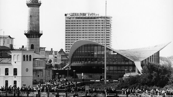 Blick auf den alten Leuchtturm und den Teepott an der Seepromenade des Ostseebades Warnemünde in Rostock, aufgenommen im Juli 1972. Dahinter ist das 1971 in Betrieb genommene Hotel "Neptun" zu sehen. Der 36,90 Meter hohe Leuchtturm wurde 1898 in Betrieb genommen, der Teepott wurde 1967 erbaut. © picture-alliance/ ZB Foto: Manfred Uhlenhut