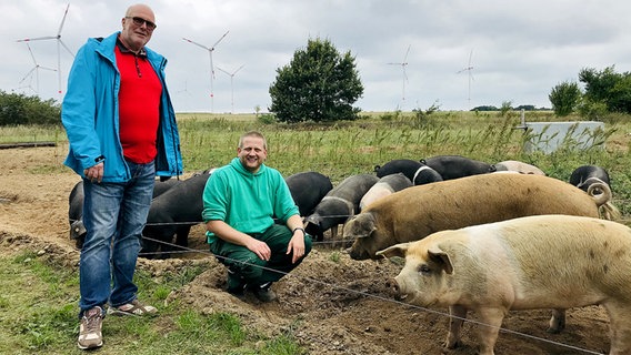 Landwirt Tino Reichelt hockt neben mehreren eingezäunten Schweinen, links neben ihm steht sein Kunde Thomas Haarweg. © NDR Foto: Franziska Drewes