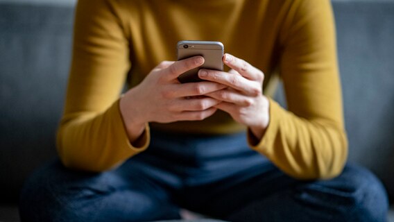 Eine Frau mit gelbem Pullover und dunklen Jeans sitz im Schneidersitz, ihr Handy in der Hand. © dpa-Bildfunk Foto: Fabian Sommer/dpa