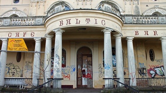 Das Portal der "Villa Baltic" mit den Aufschriften "Cafe" und "Bar" zeigt deutliche Spuren des Verfalls, unter dem Säulengang sind die Wände mit Graffiti beschmiert. © NDR.de Foto: Daniel Sprenger