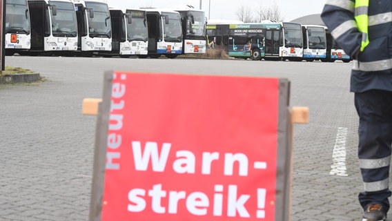 Ein Schild mit der Aufschrift "Warnstreik" steht auf dem Hof eines Bus-Depots. © dpa Foto: Stefan Sauer