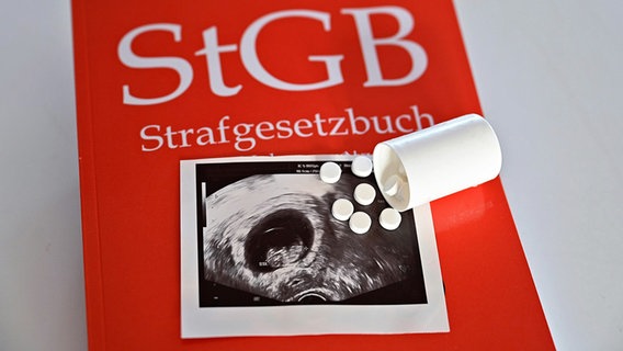 Ein Ultraschallbild mit Tabletten liegt auf einem Strafgesetzbuch. © picture alliance / epd-bild Foto: Heike Lyding